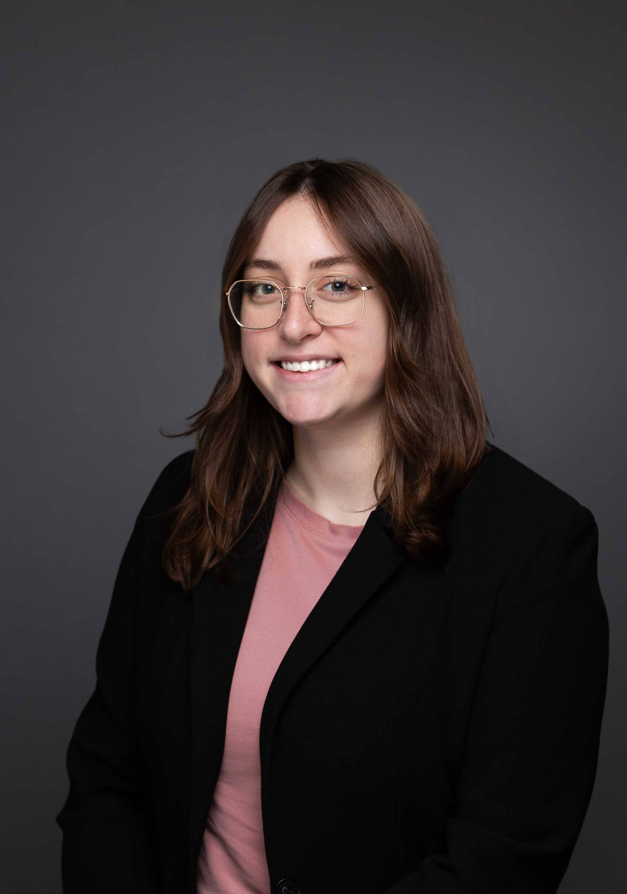 Sam Kiel in a black blazer with a peach blouse on wearing a necklace and glasses.